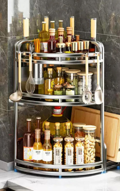 Multi-tiered kitchen storage rack with bottles and kitchen utensils on a gray marble countertop.