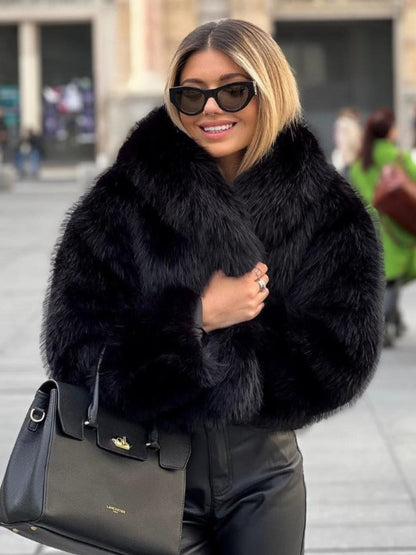 Woman wearing a black fur coat and sunglasses, holding a black handbag.