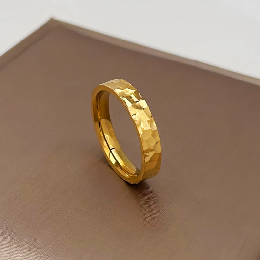 Gold ring with a textured design on a brown surface