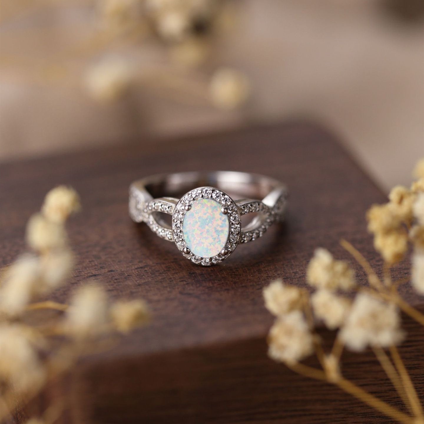 Silver ring with a central gemstone on a wooden surface with dried flowers.