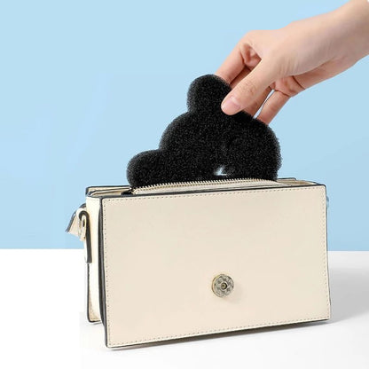 A black sponge shaped like a bear is shown being used to pick up pet hair from a beige surface, demonstrating its use as a cleaning tool.