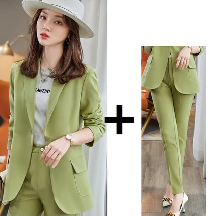 Woman wearing a green blazer coat and pants with a white shirt underneath, standing indoors.