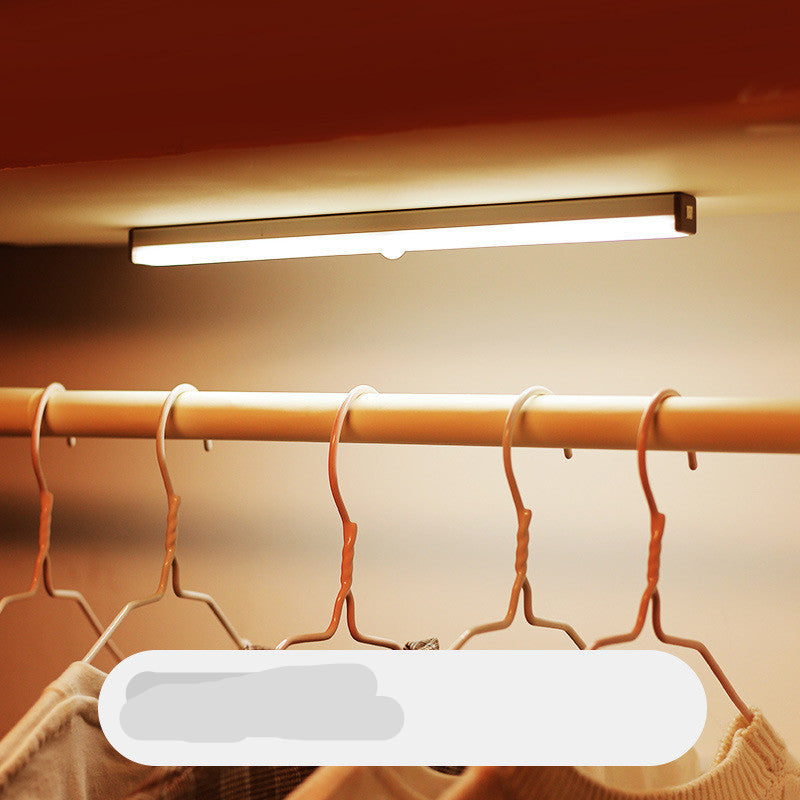 Under-cabinet LED light fixture above a clothing rack with hangers.