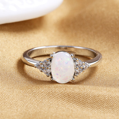 Silver ring with a white opal stone on a gold fabric background