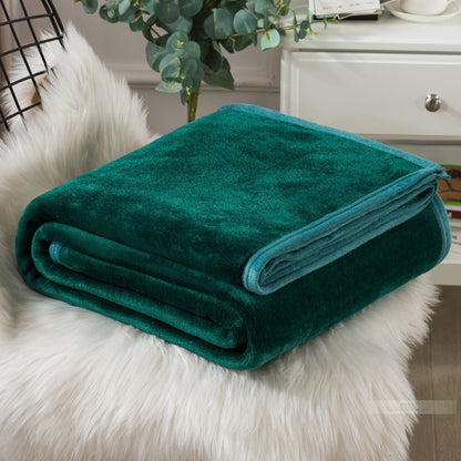 A blue coral fleece blanket placed on a white furry surface, with a part of a bed and a plant in the background.