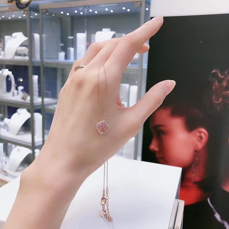 Hand wearing a gold necklace with a heart pendant, blurred background