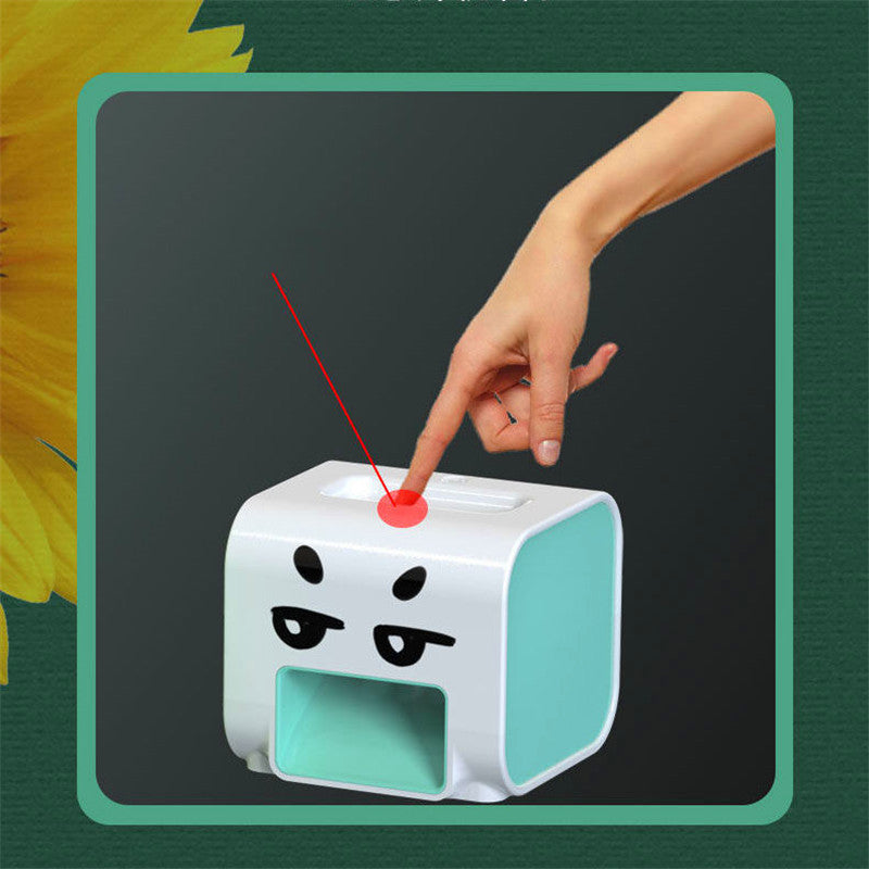 Hand pressing a red button on a white and green device with a cartoon face design.