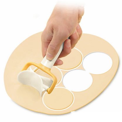 Hand using a cookie cutter on a round wooden board with circular cutouts.