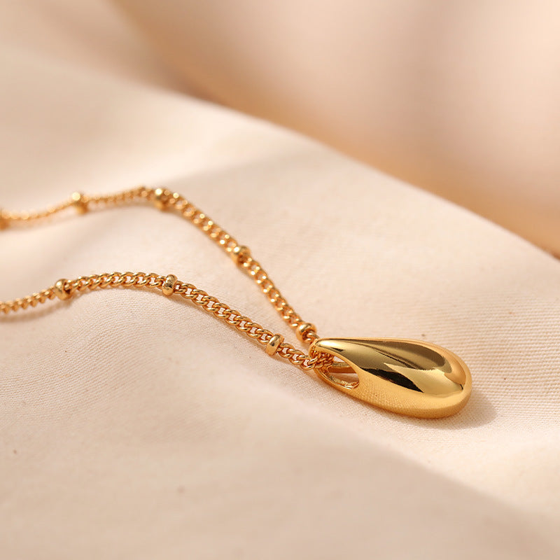 Gold necklace with a teardrop pendant on a beige background