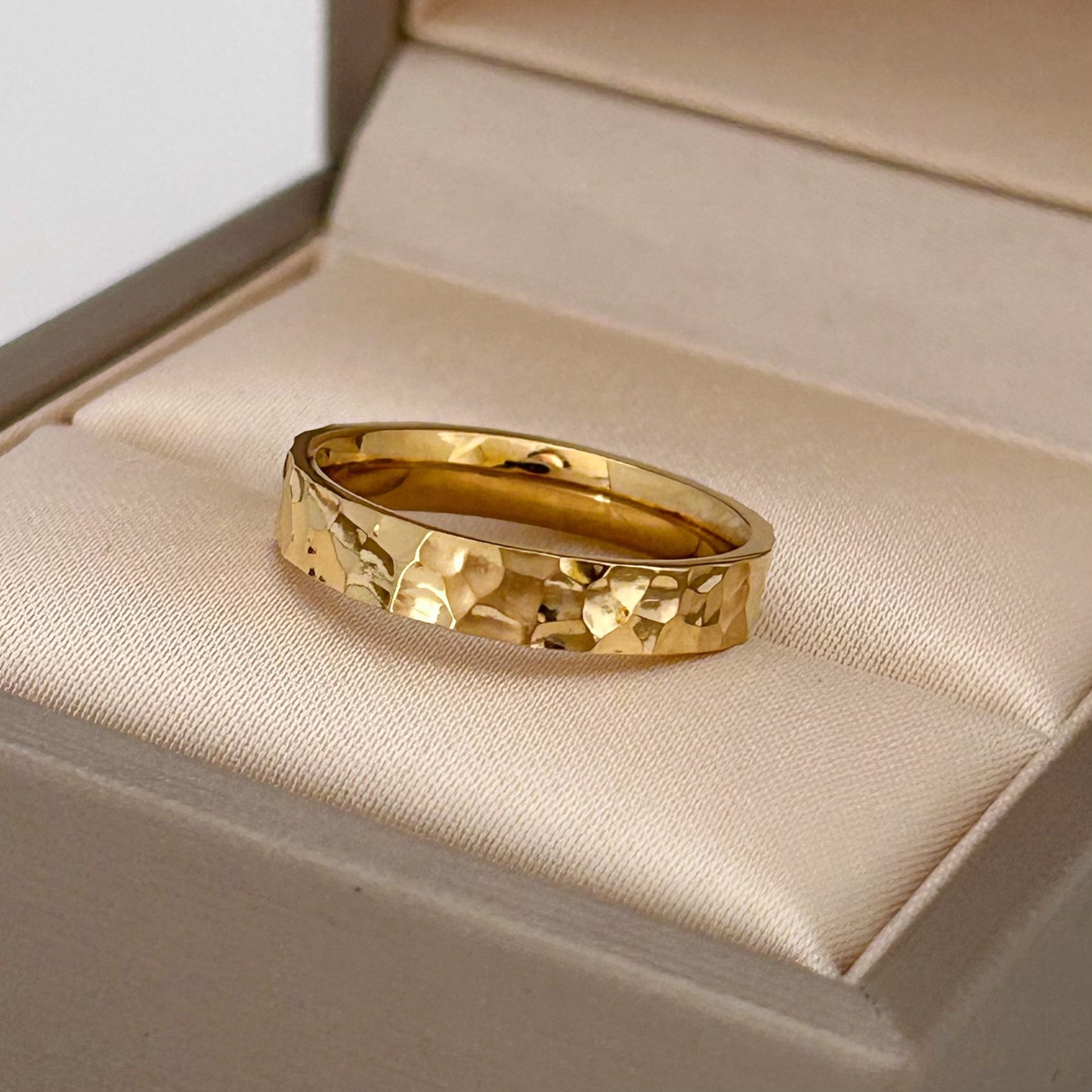 Gold ring with a textured design on a beige cushion in an open jewelry box.