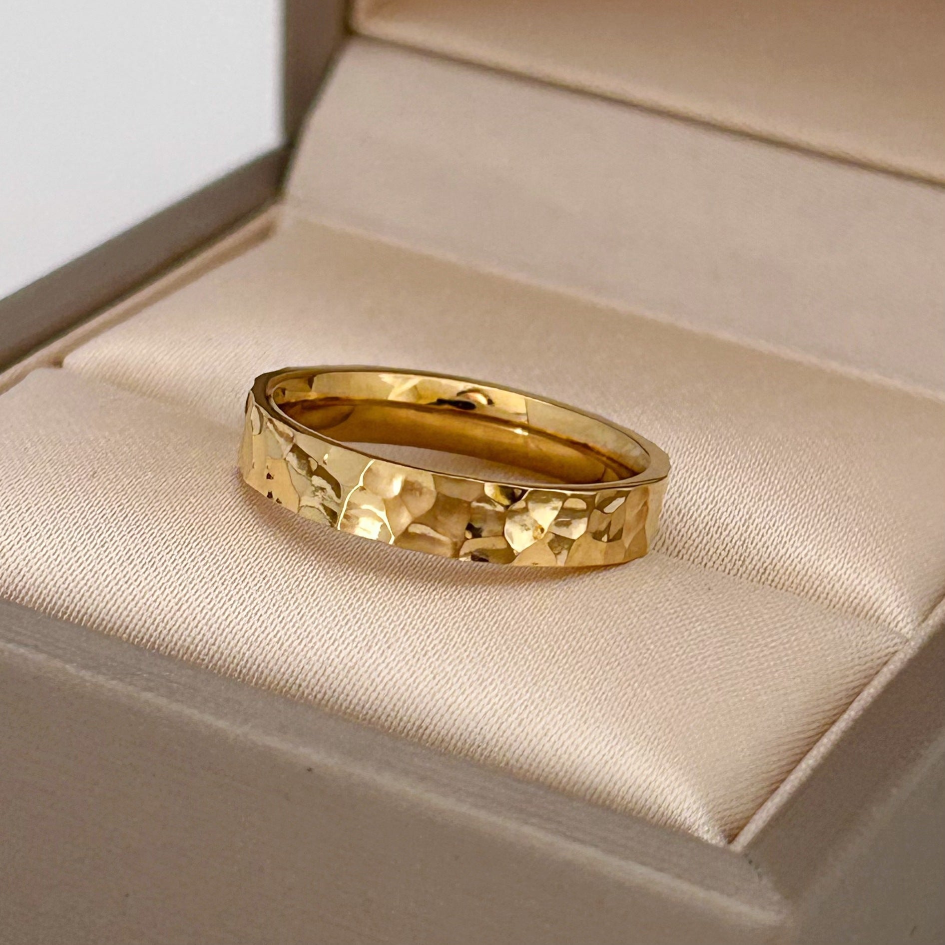 Gold ring with a textured design on a beige cushion in an open jewelry box.
