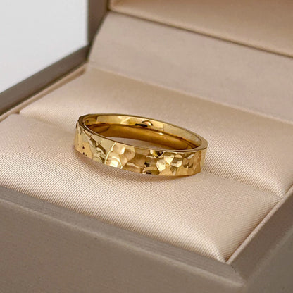 Gold ring with a textured design on a beige cushion in an open jewelry box.