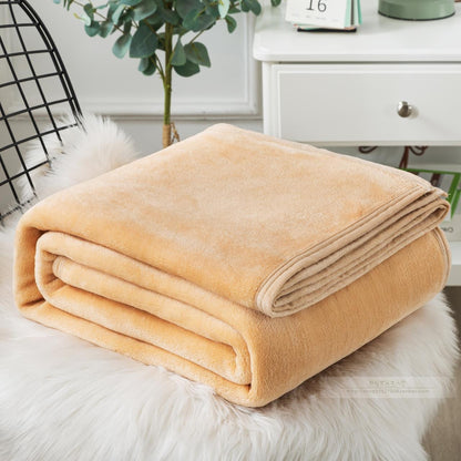 A blue coral fleece blanket placed on a white furry surface, with a part of a bed and a plant in the background.