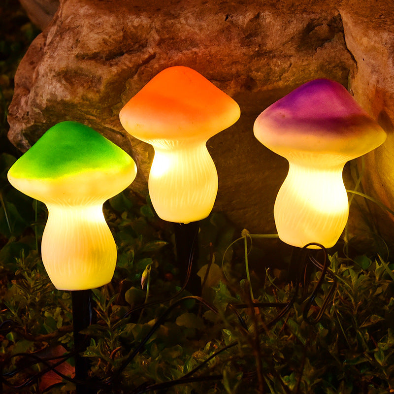 Three colorful mushroom-shaped lights on stakes in a garden setting with rocks in the background.