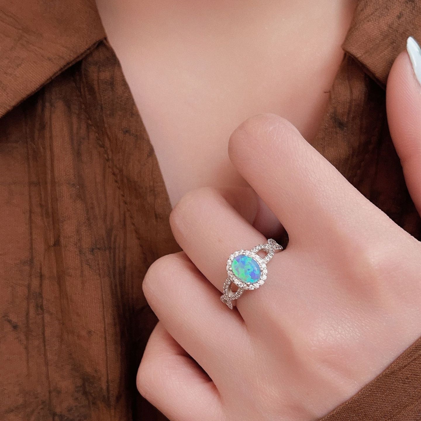 Close-up of a hand wearing an opal ring with a brown background