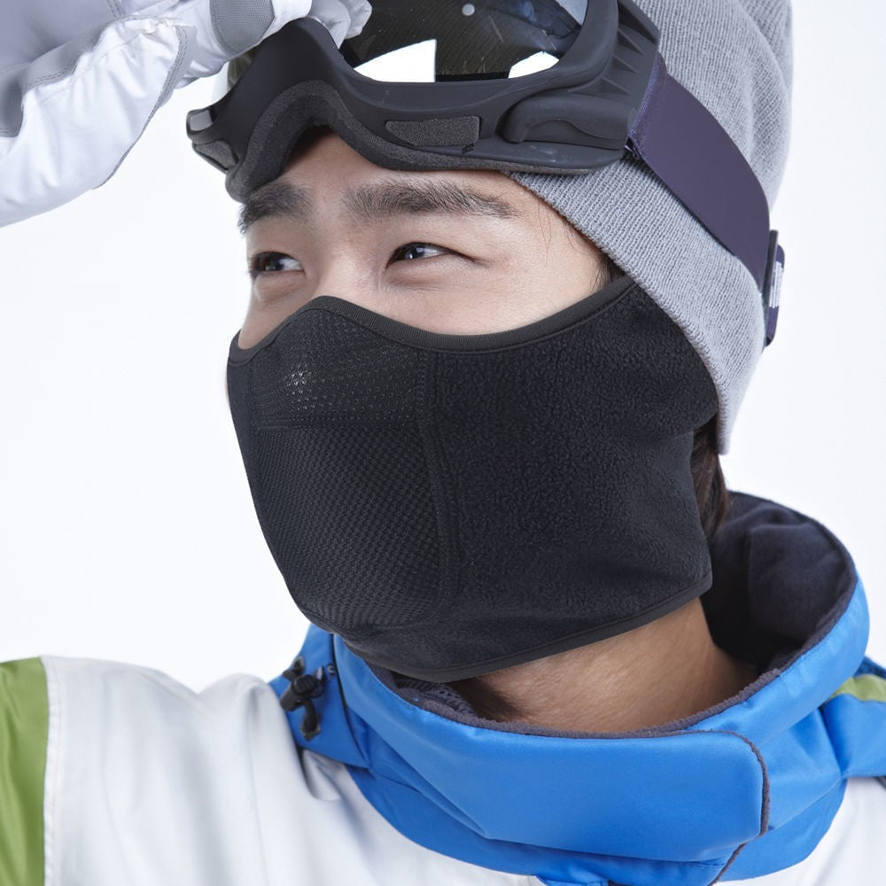 Person wearing a black face mask, goggles, and winter clothing on a white background