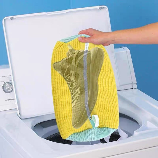 A shoe being washed in a yellow laundry bag with a grey zipper, placed in a washing machine.