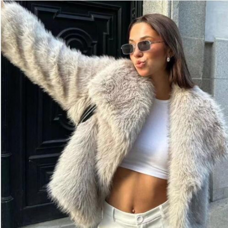 Woman wearing a fluffy white coat and sunglasses, standing in front of a building entrance.