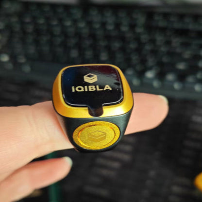Black and gold device with 'iQIBLA' branding held by a hand on a blurred keyboard background