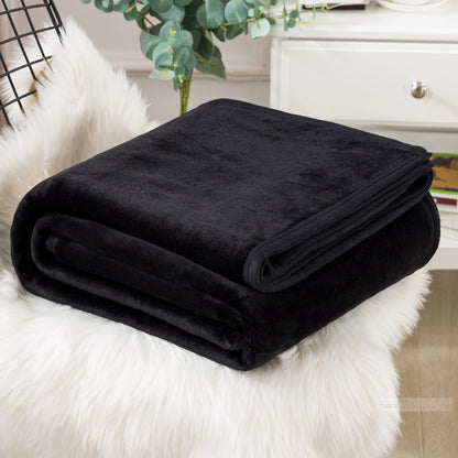 A blue coral fleece blanket placed on a white furry surface, with a part of a bed and a plant in the background.
