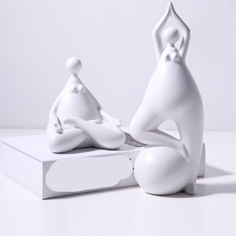 A pair of white ceramic figurines, one sitting and one standing, placed on top of a stack of books with a decorative vase beside them.