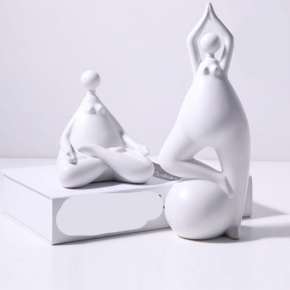 A pair of white ceramic figurines, one sitting and one standing, placed on top of a stack of books with a decorative vase beside them.