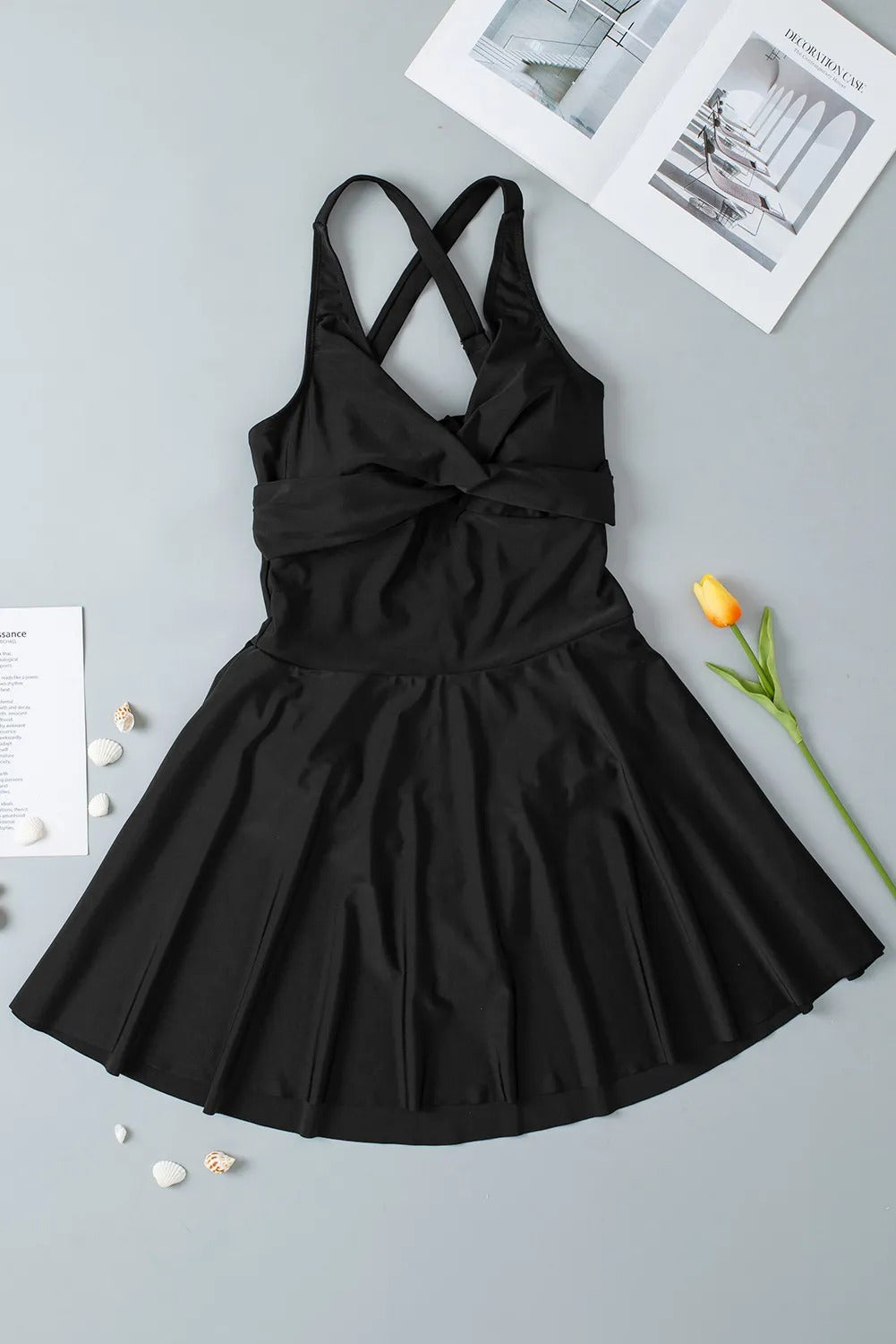 Black dress with criss-cross straps on a gray surface with a flower and paper.