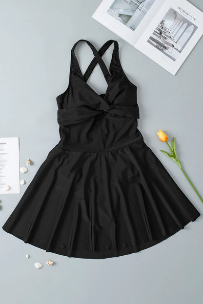 Black dress with criss-cross straps on a gray surface with a flower and paper.