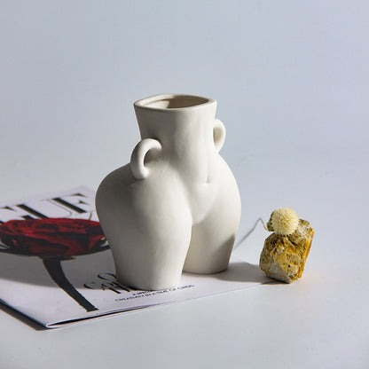 A black ceramic gourd-shaped vase on a white surface, with a bouquet of multicolored flowers arranged in it, placed against a neutral background with a grey sofa.