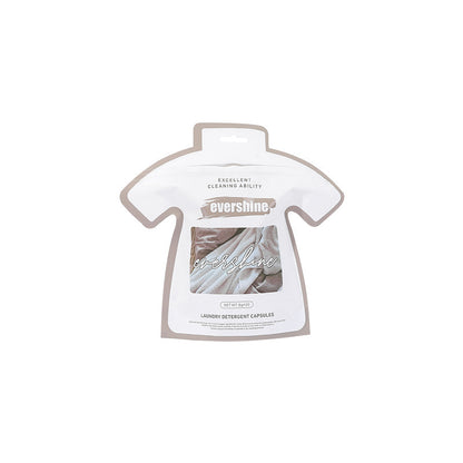 Packaging of laundry gel beads in the shape of a shirt placed on a washing machine, with plants and laundry in the background.