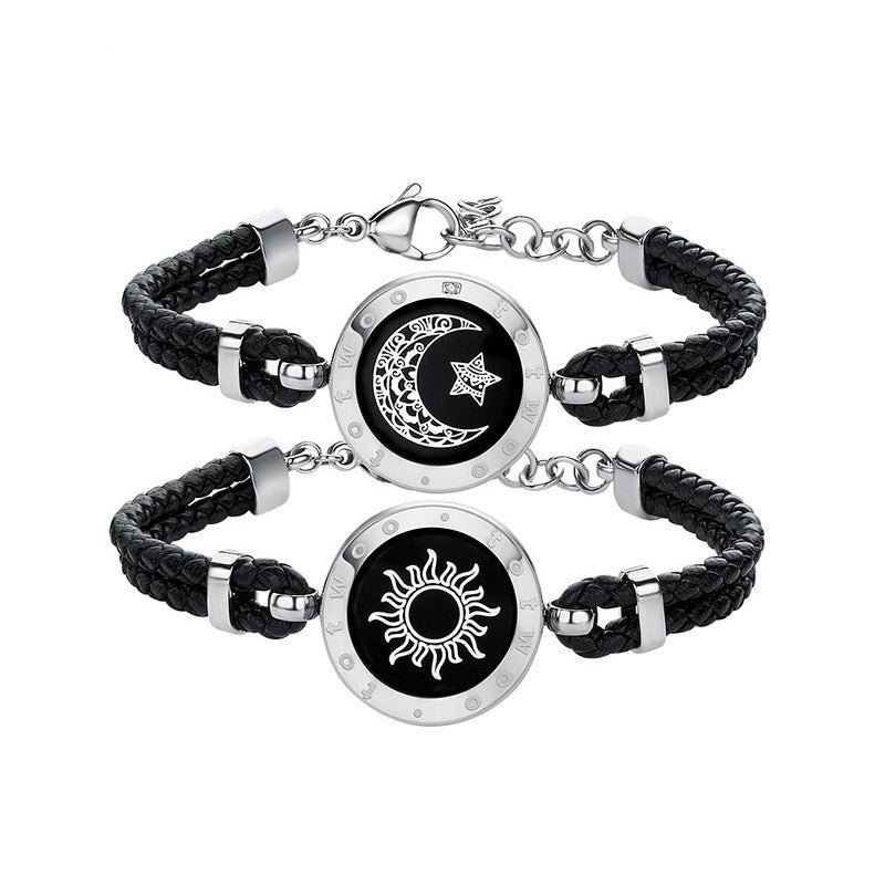 Pair of black braided bracelets with silver circular charms featuring celestial designs on a white background.