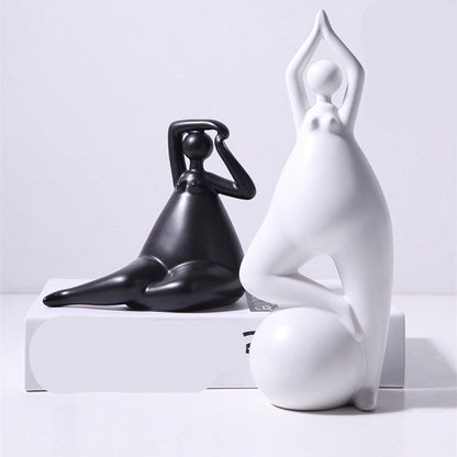 A pair of white ceramic figurines, one sitting and one standing, placed on top of a stack of books with a decorative vase beside them.