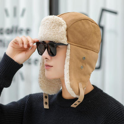 Person wearing a tan aviator hat with ear flaps and holding sunglasses, against a blurred background.