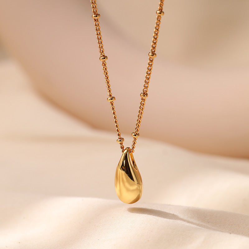 Gold necklace with a teardrop pendant on a beige background