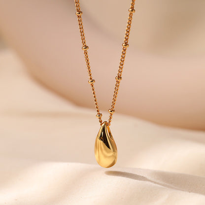 Gold necklace with a teardrop pendant on a beige background