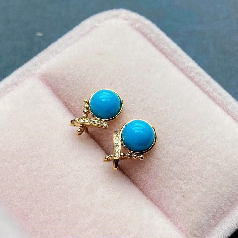 Turquoise earrings with gold accents on a pink cushion