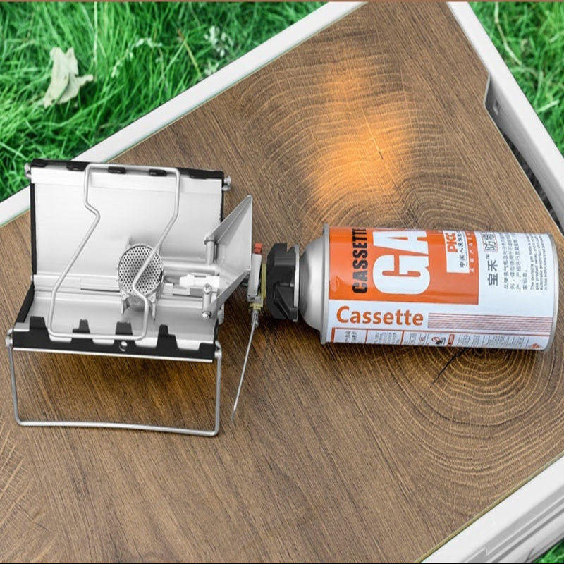 Portable camping stove with a canister on a wooden surface outdoors.