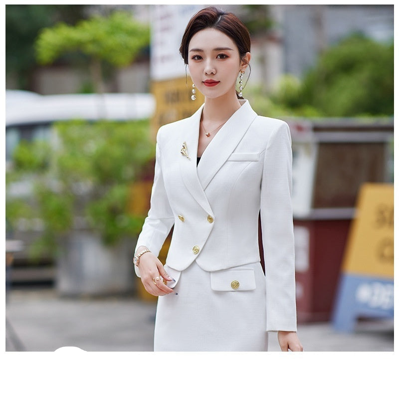 A woman in a white leisure formal suit with a blazer and a skirt, featuring long sleeves and gold buttons, standing outdoors.