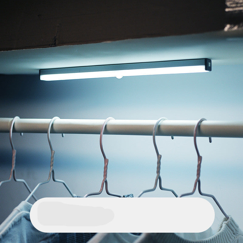 Under-cabinet LED light bar illuminating a clothing rack with hangers.