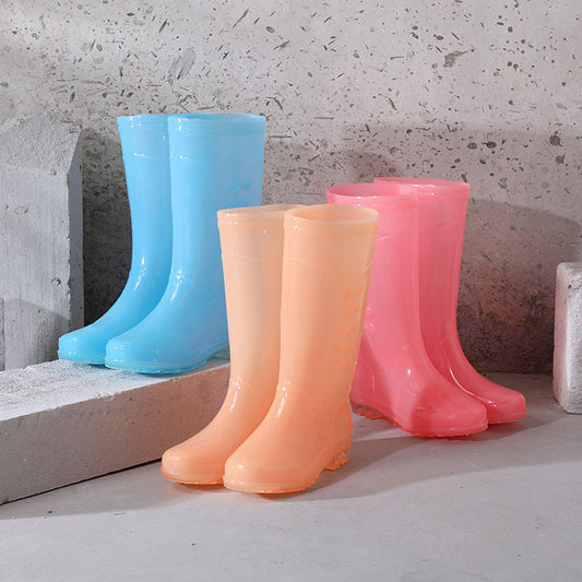 Three colorful rubber boots (blue, peach, pink) on a concrete surface.