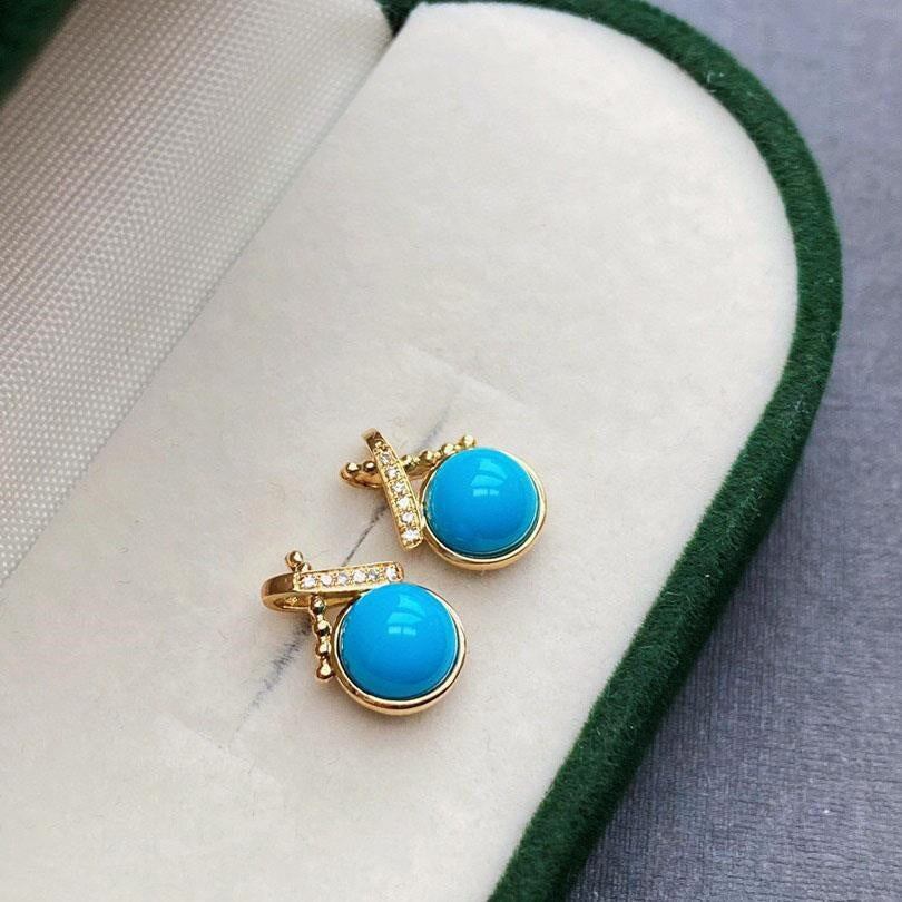 Pair of turquoise earrings with gold accents on a white cushion