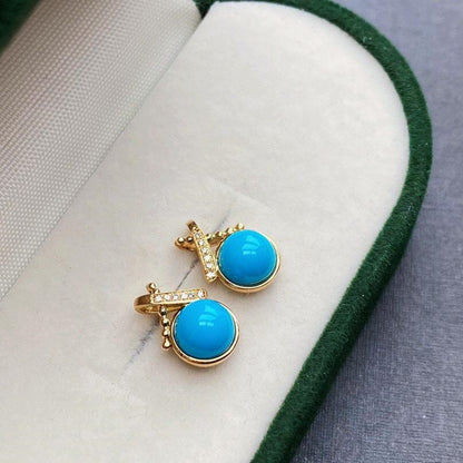 Pair of turquoise earrings with gold accents on a white cushion