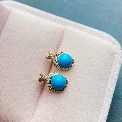 Turquoise earrings with gold accents on a pink surface