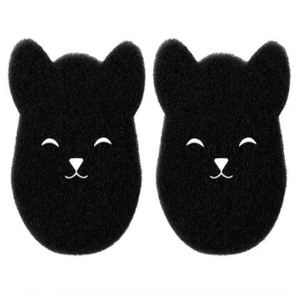 A black sponge shaped like a bear is shown being used to pick up pet hair from a beige surface, demonstrating its use as a cleaning tool.