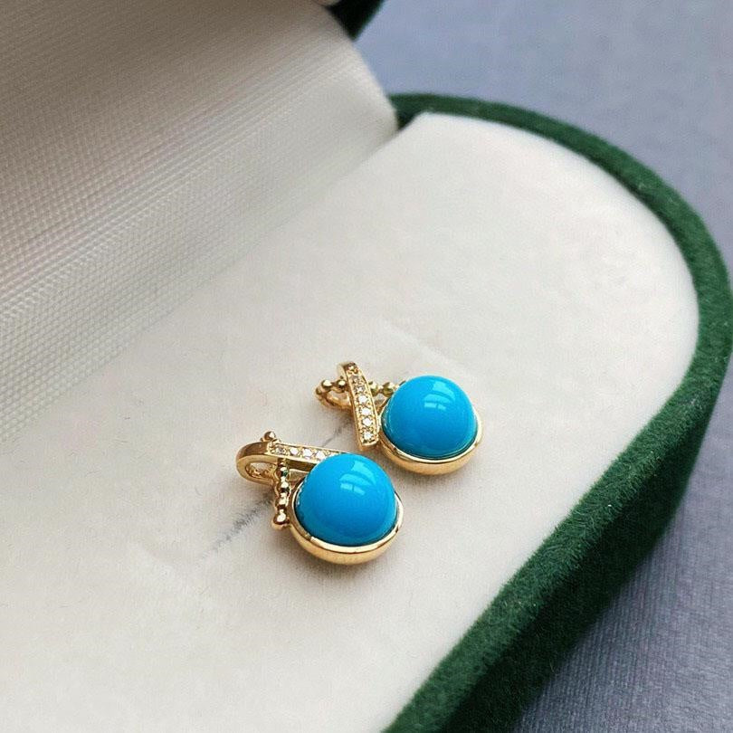 Gold earrings with turquoise stones on a white and green fabric background