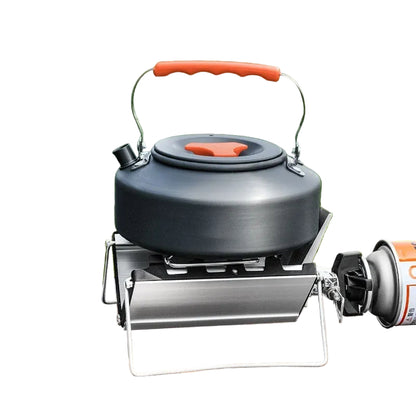 Black camping kettle with red handle on a stove over grass background