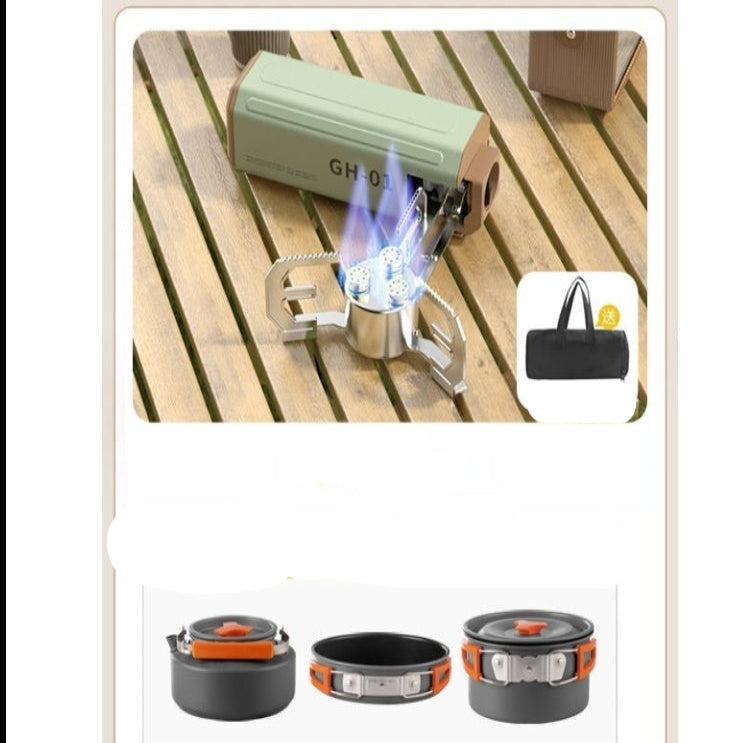 Portable cassette stove with flames on a wooden surface, surrounded by cooking utensils and a storage bag.