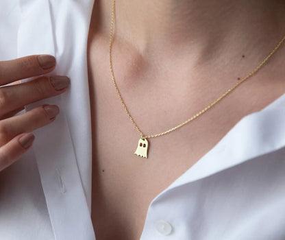 Gold necklace with a ghost pendant worn by a person in a white shirt.