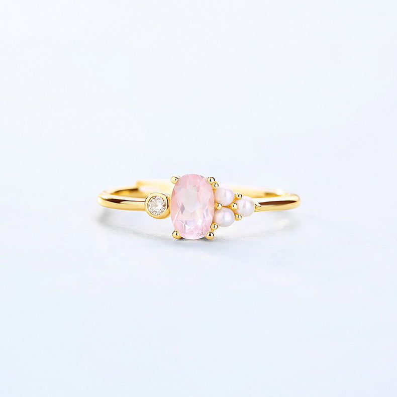 Gold ring with a pink gemstone and pearls on a light gray background