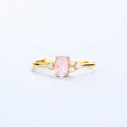 Gold ring with a pink gemstone and pearls on a light gray background